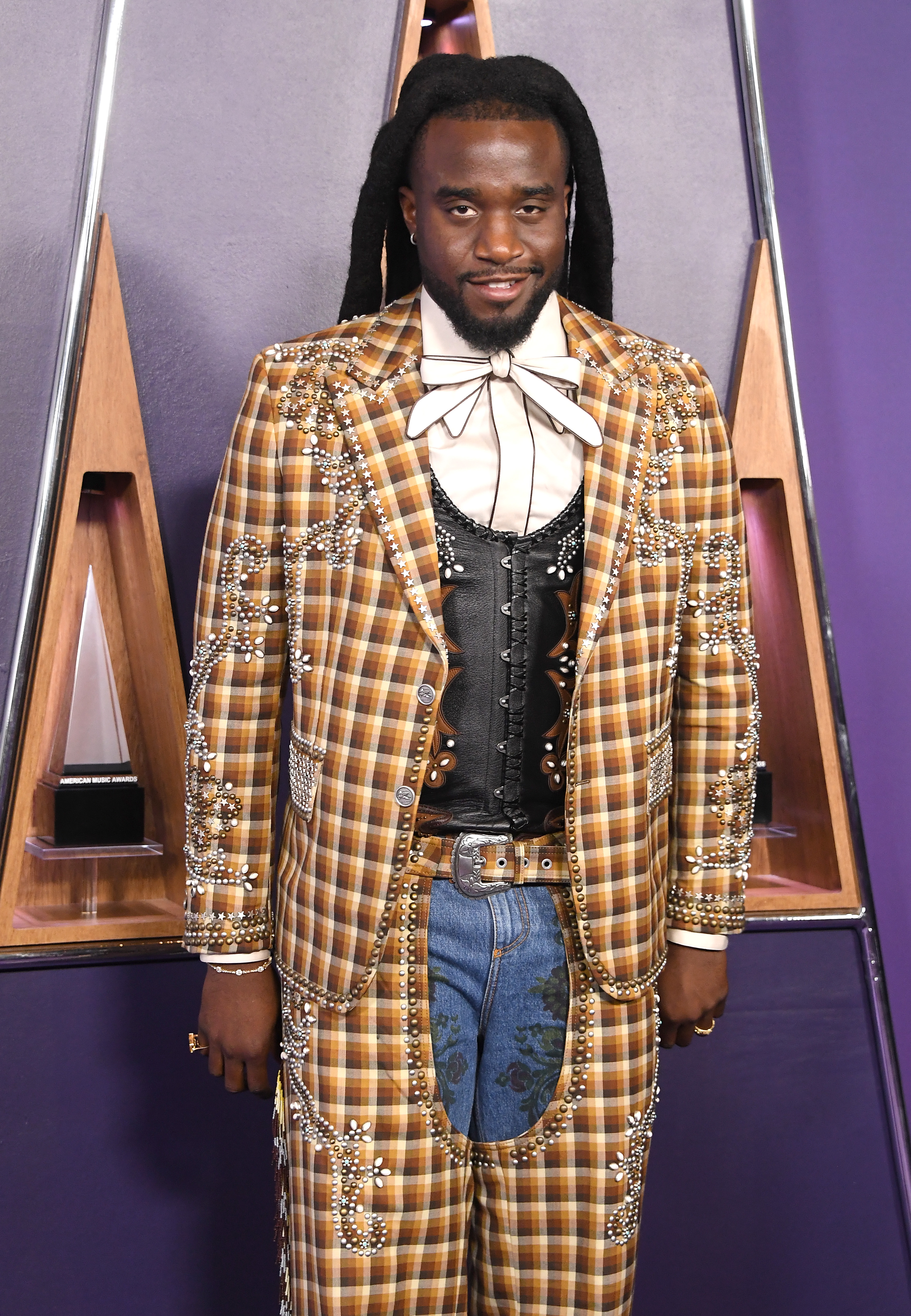 Dressed in a mustard plaid suit accented with rhinestone stars, Shaboozey layered the look over a black embroidered waistcoat and crisp shirt. His mix of textures gave cowboy couture a red carpet-ready twist.