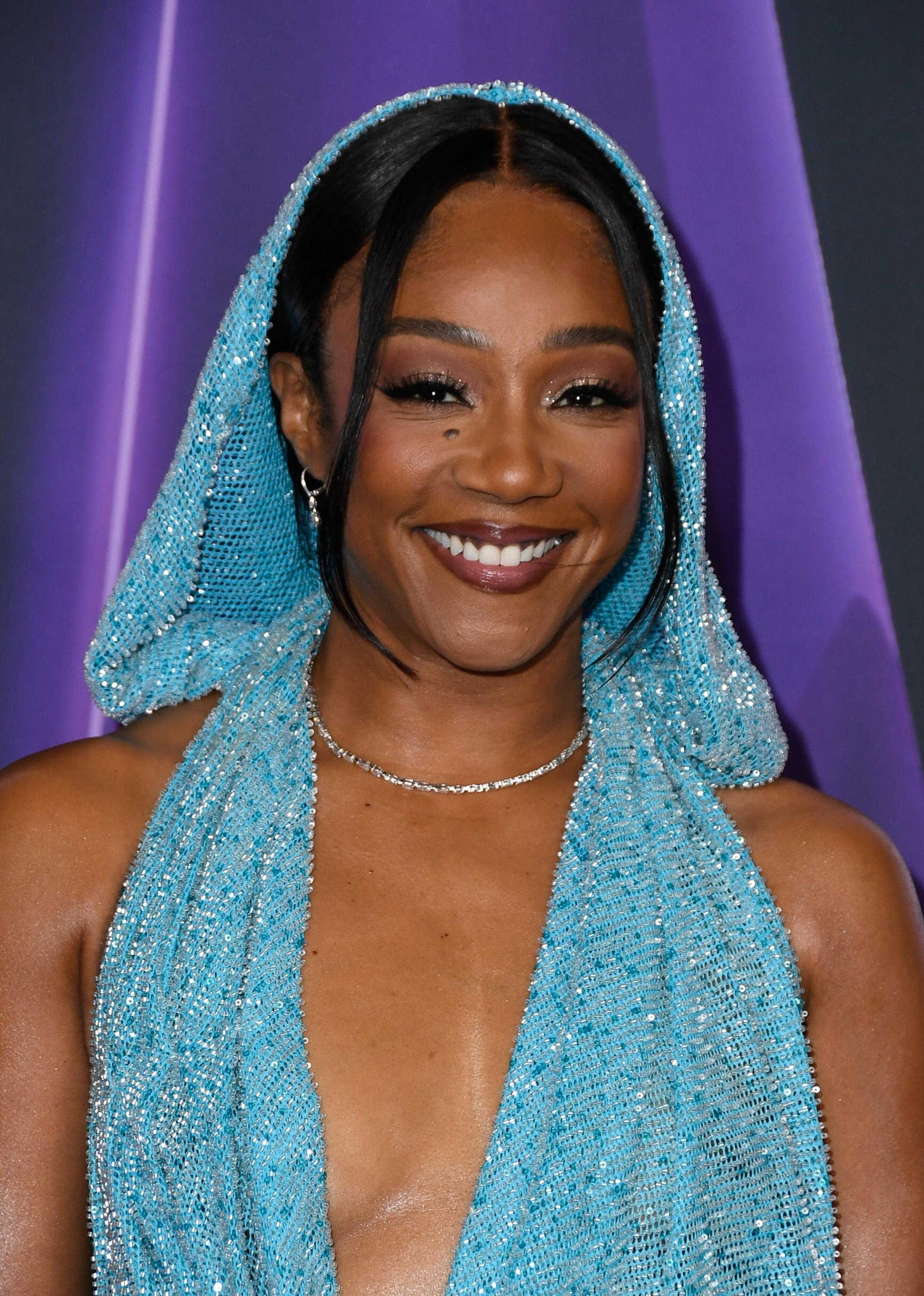 Tiffany Haddish at the 2025 AMAs wore a shimmering blue halter gown with a matching hood. The glittering fabric complemented her center-part hairstyle, paired with subtle jewelry and a classic lipstick shade.