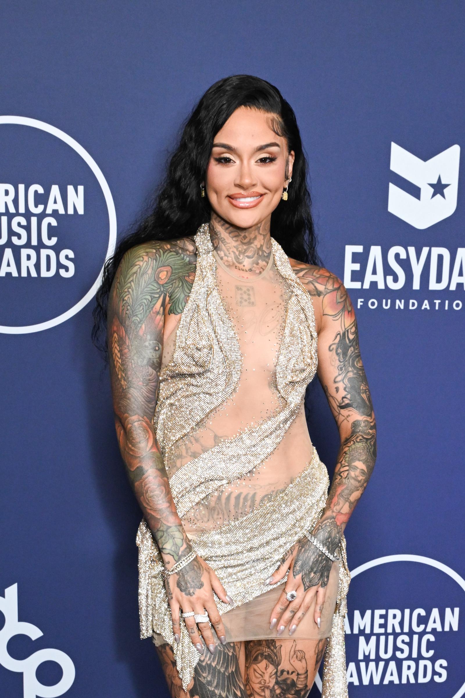 Kehlani brought shimmer and edge to the 2025 AMAs in a sheer mesh gown with asymmetrical silver paneling that zigzagged across her torso. Bold styling and translucent fabric left little to the imagination, spotlighting her tattoos with fearless flair.