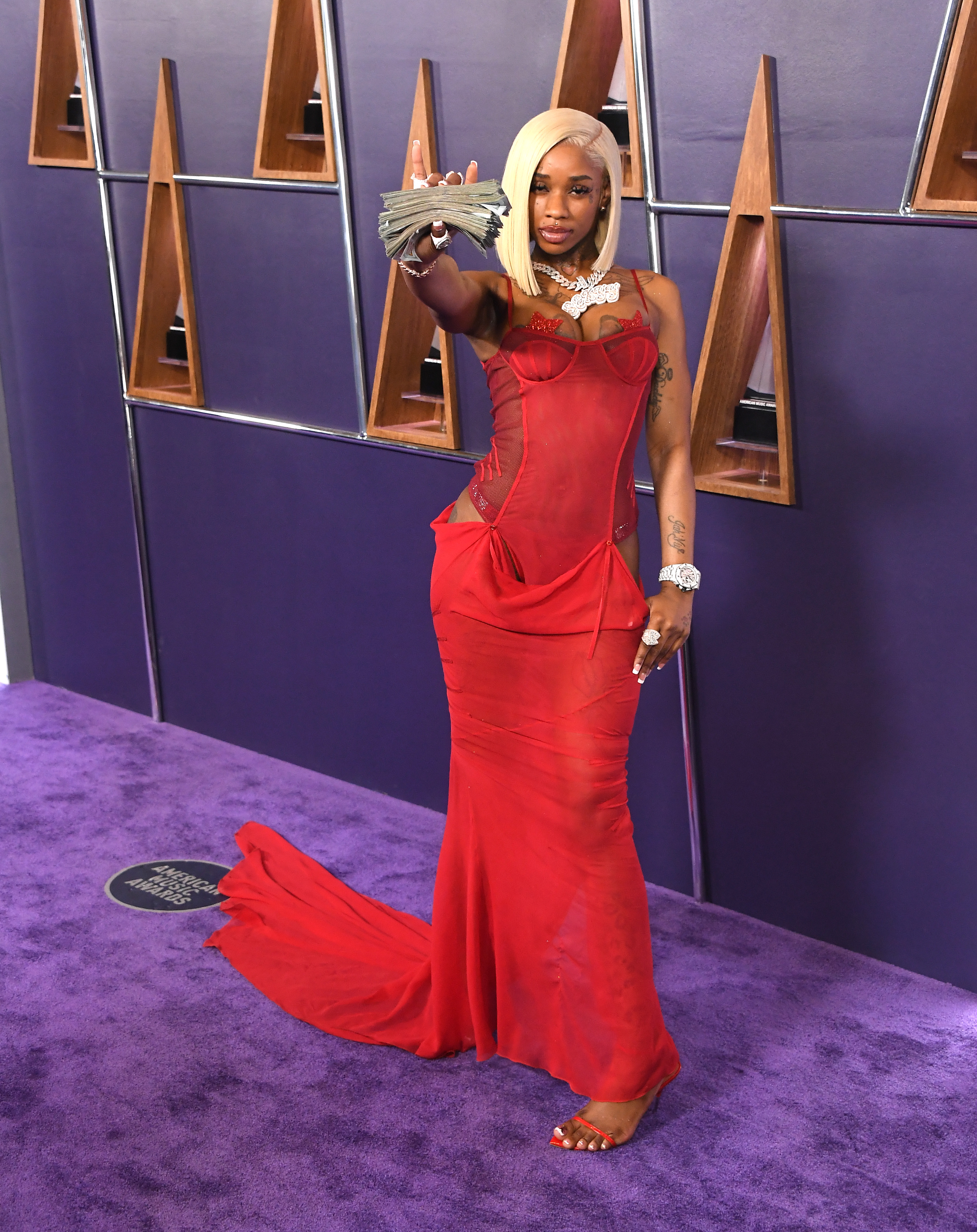 On the purple carpet, Sexyy Red made a scene-stealing entrance in a form-fitting red corset gown with sheer mesh panels and a dramatic train. A fan of cash and icy wristwear gave the whole moment a signature, unapologetic twist.