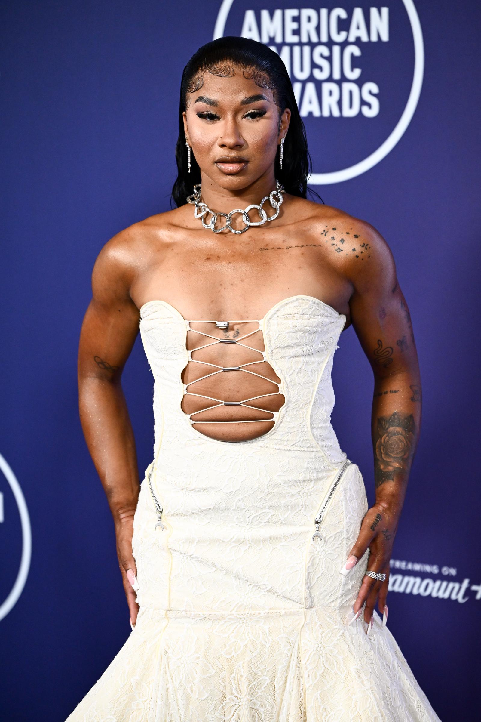 Jordan Chiles brought bold structure to the 2025 AMAs with edgy metallic accents and sharp contouring on her corset bodice. Her chunky silver chain necklace and sleek, wet-look hair added a modern, athletic-chic twist to the red carpet glam.