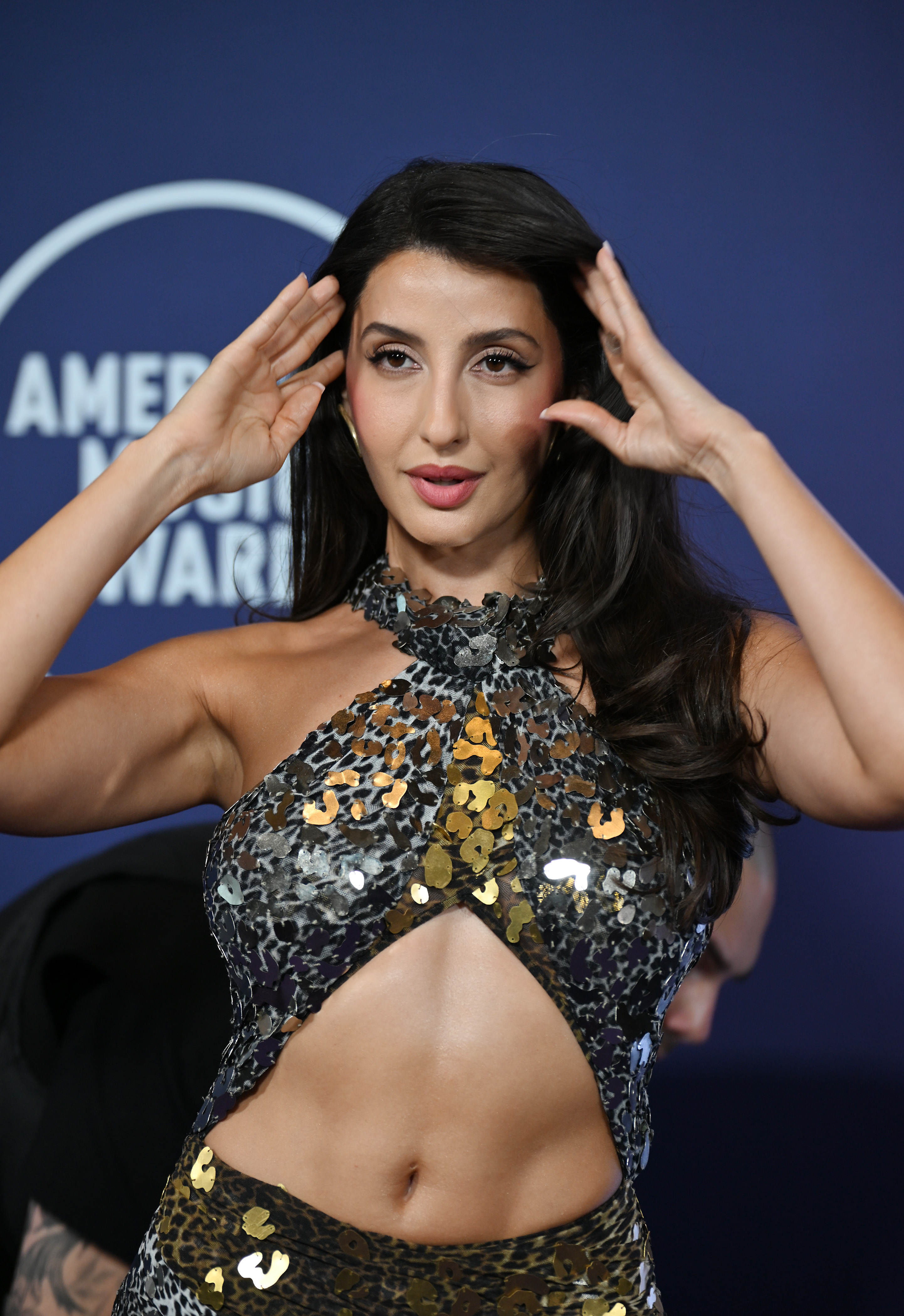 At the 2025 AMAs, Nora Fatehi's sequined gown showcased a cutout bodice and bold animal print. The layered paillettes in silver and gold added contrast against the printed fabric's darker base.