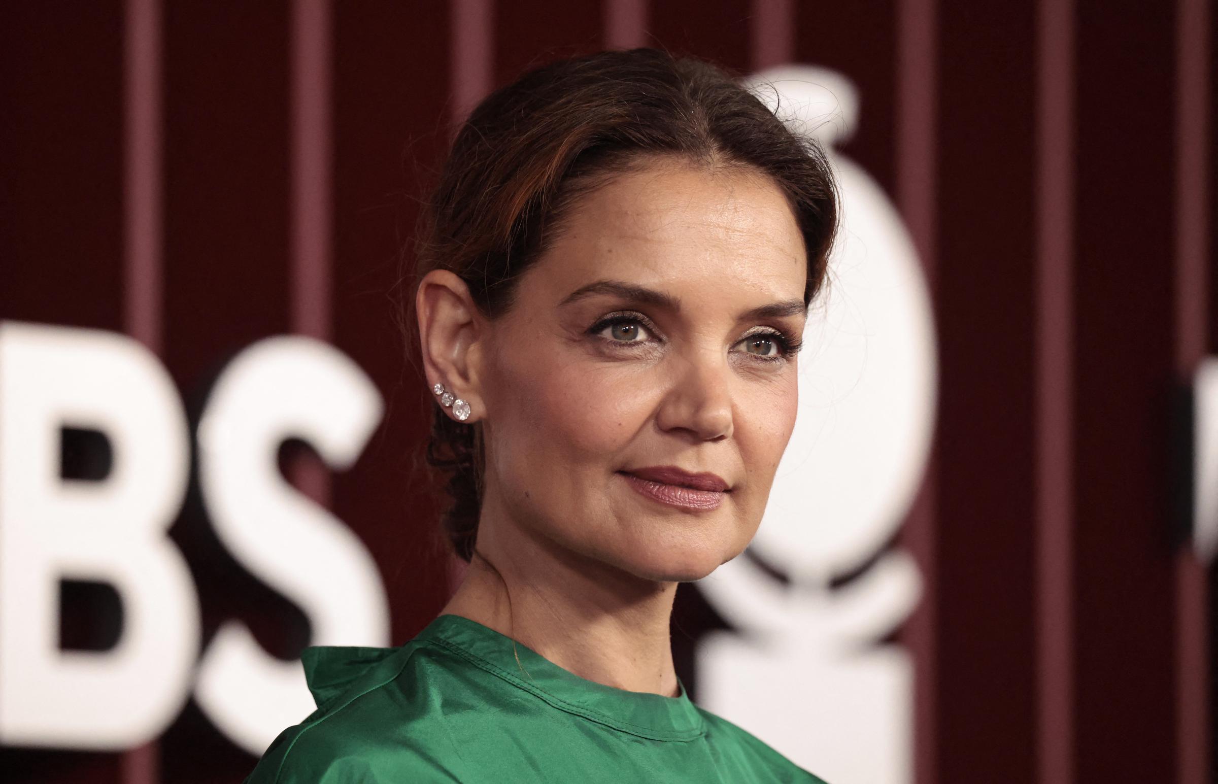 With her hair in a sleek updo and glowing makeup, Katie Holmes brings understated elegance to the red carpet, pairing a bold green satin top with sparkling earrings and a soft, confident gaze.